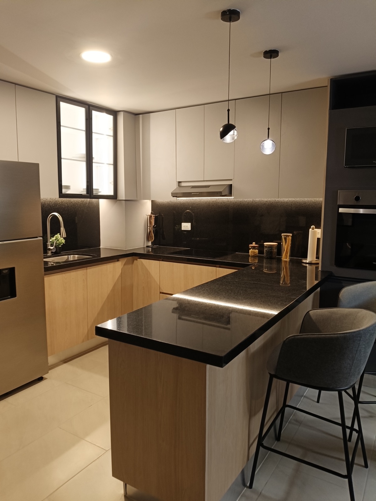 Cocina con barra de cubierta negra, lámparas colgantes, bancos y gabinetes en madera clara