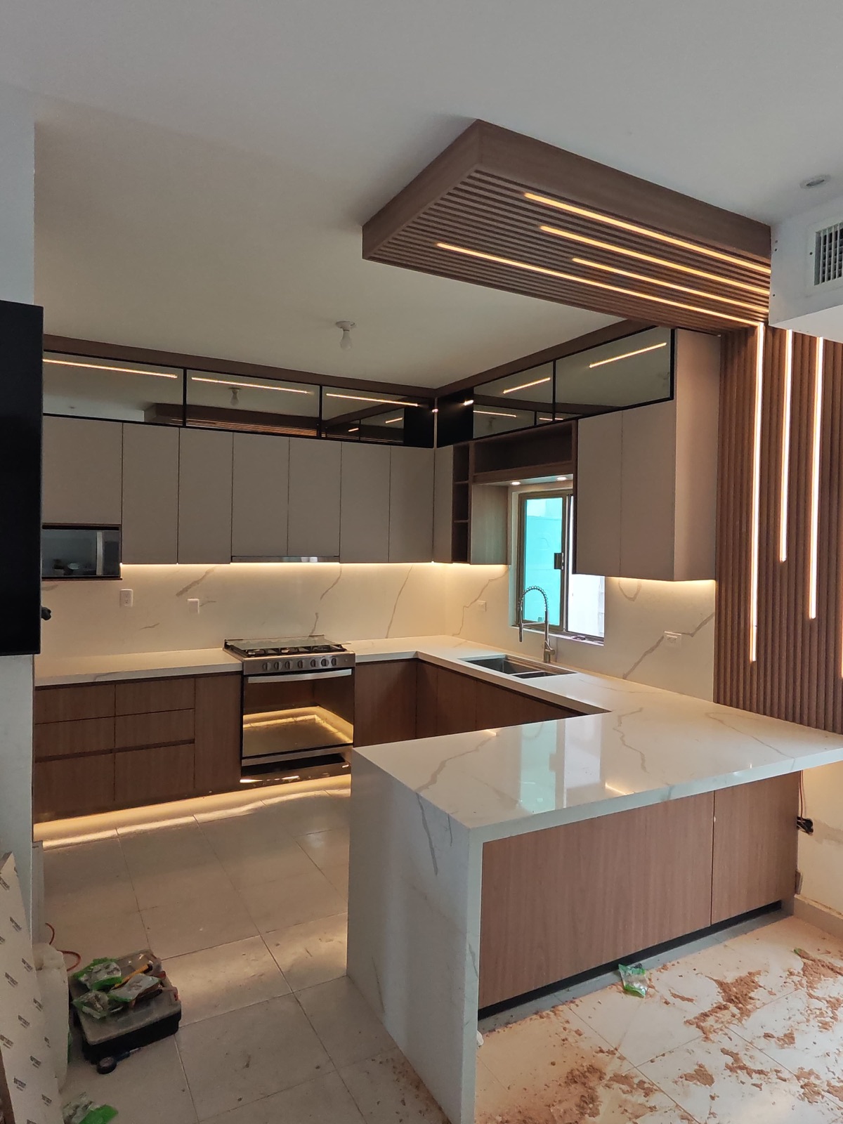 Vista amplia de cocina con celosía de madera iluminada, cubierta de mármol blanco y zoclo con luz LED