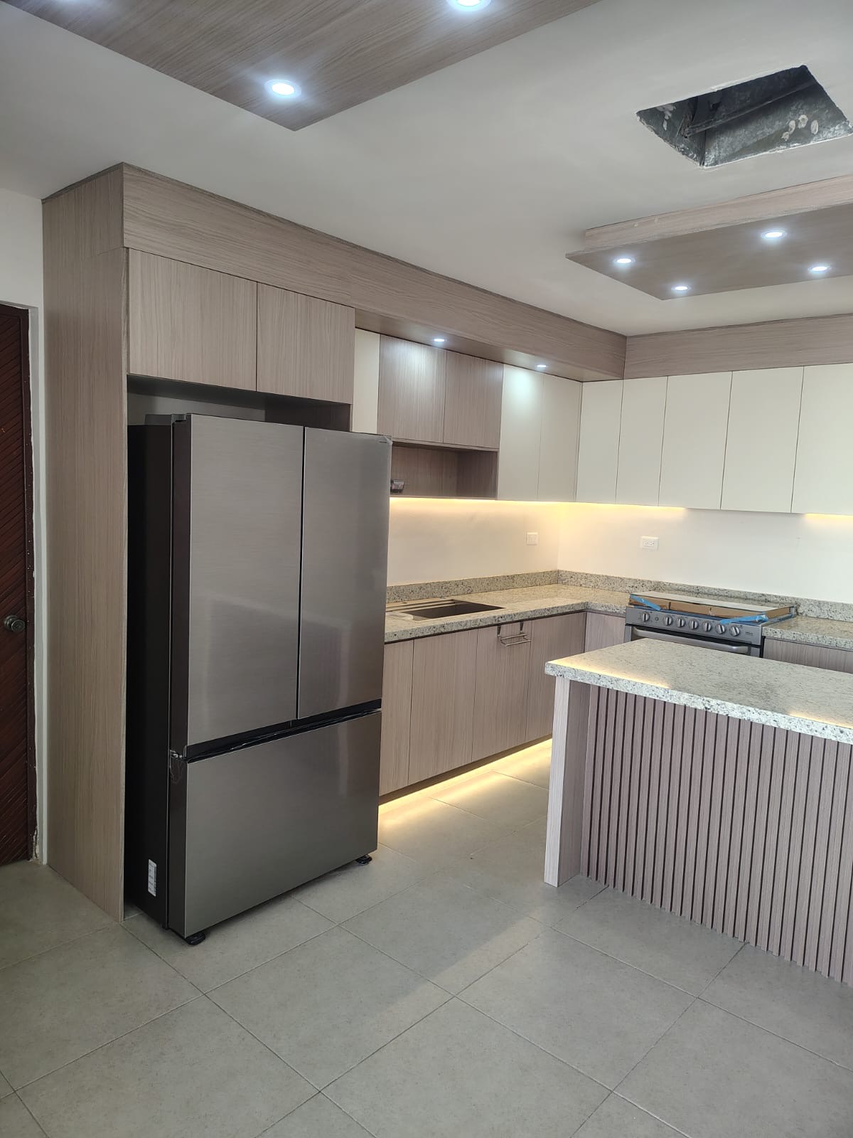 Cocina en tonos madera con refrigerador integrado e isla de granito con celosía