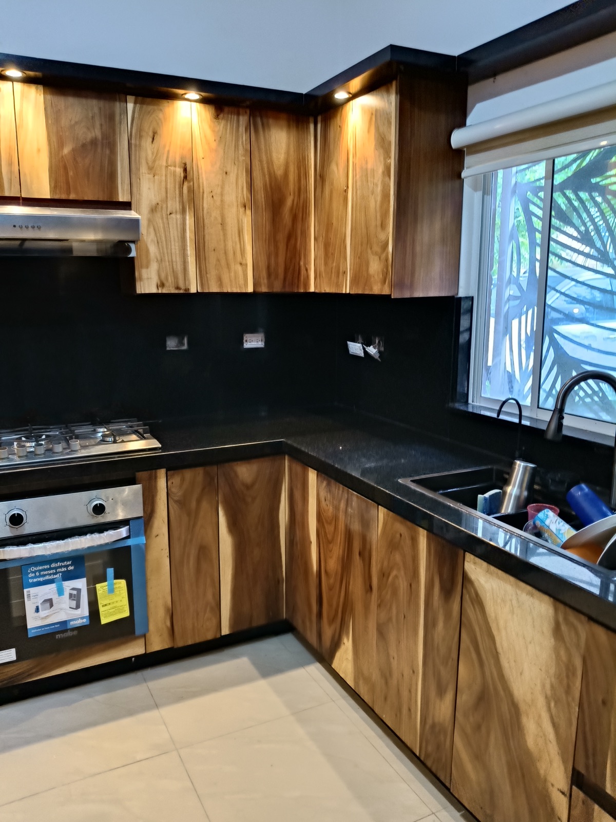 Cocina de madera natural con veta marcada, cubierta negra e iluminación puntual