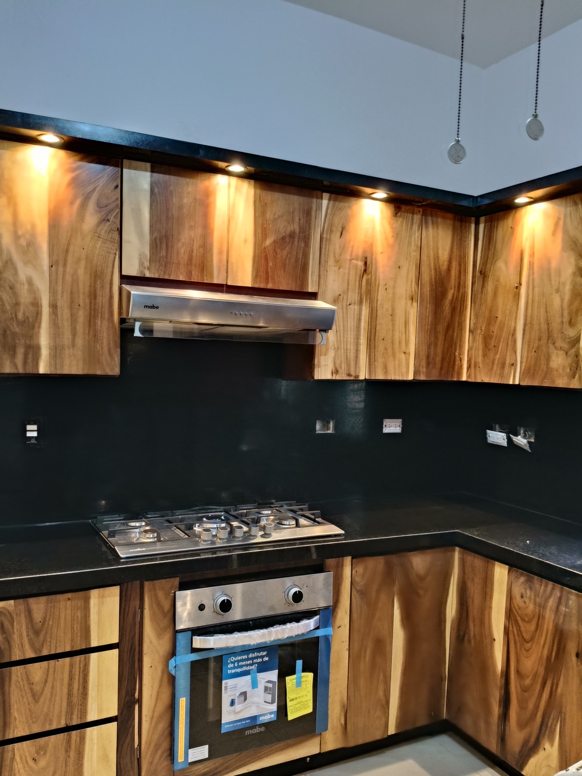 Gabinetes de madera natural tipo parota con luces empotradas y cubierta de granito negro