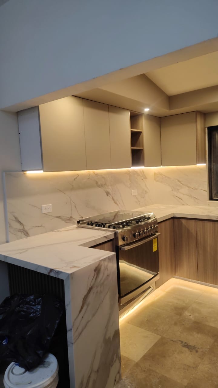 Cocina con mármol cálido, alacenas en tono arena y luz LED bajo gabinete